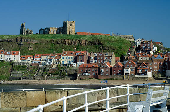 ENG: Yorkshire & Humberside Region, North Yorkshire, North Yorkshire Coast, Whitby, West Pier, Houses bunch beneath cliffs at the mouth of the harbor; people climb the Abbey Steps to Whitby Abbey [Ask for #270.162.]