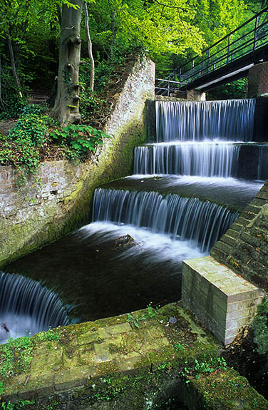 WAL: Flintshire County, Clwydian Hills, Holywell, Greenfields Valley Heritage Park. Water cascades over a mill pond's brick weir, in these ruins from an 18th C. copper rolling plant, now in a forest. [Ask for #246.070.]