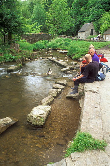 ENG: West Midlands Region, Staffordshire, Peak National Park, The River Dove, Milldale, Walkers relax by the River Dove in the center of the village, a medieval packhorse bridge in the bkgd [Ask for #246.288.]