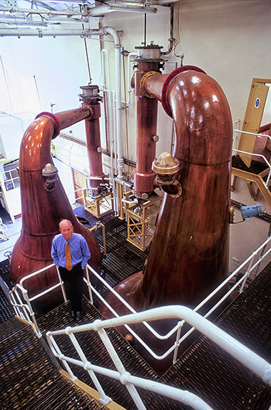 SCO: Argyll & Bute , Inner Hebrides, Islay, Port Askaig Area, Bunnahabhain Distillery. Interior of stillhouse -- John McClellen, distillery manager, stands on catwalk in front of stills [Ask for #246.437.]