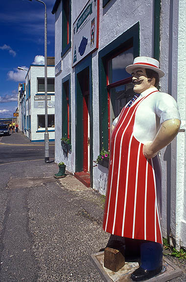 SCO: Argyll & Bute , Inner Hebrides, Islay, Bowmore, Entrance to butcher shop in the center of town, with statue of butcher; street slopes down to the harbor. [Ask for #246.444.]