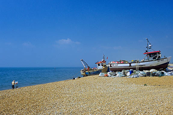 ENG: South East Region, Kent, Romney Marsh, Romney Marsh Beaches, Fishing boats drawn up on the shingle beach; man on boat with net; a woman artist paints the scene [Ask for #256.500.]